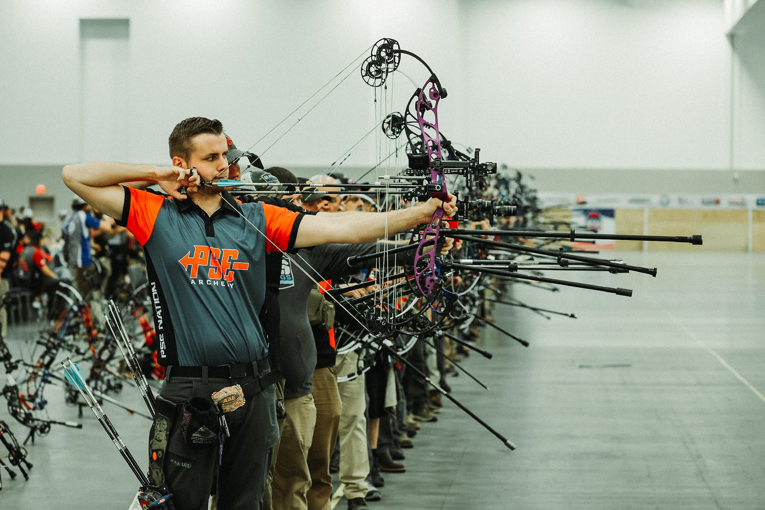 Competitive target archers at an indoor competition. PSE jersey on the first shooter.