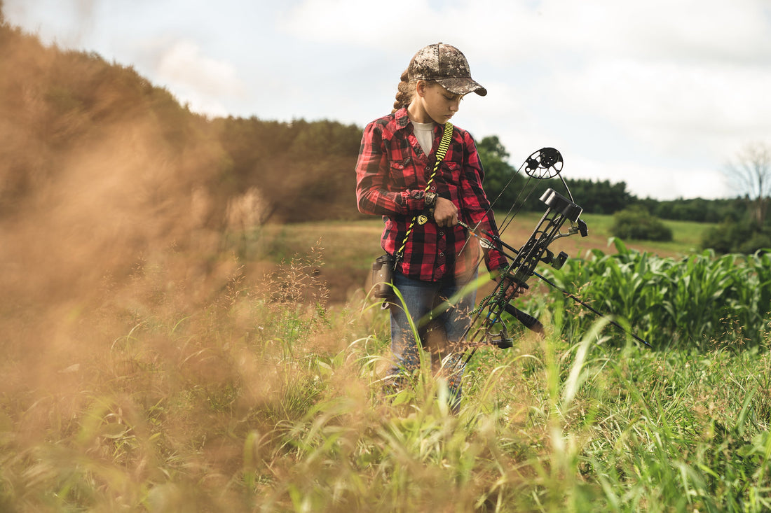 Photo of a young girl in black and red plaid shirt holding a PSE kid's bow.
